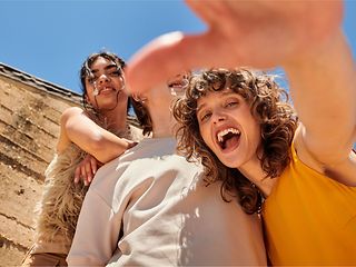 Drei ausgelassene junge Menschen posieren unter blauem Himmel für ein Selfie.