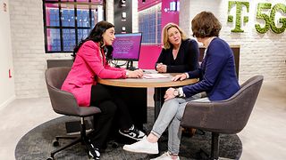 Three people sit at a table talking with one another