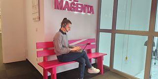 Volontärin sitzt mit Headset auf einer Bank und arbeitet am Laptop auf dem Schoß