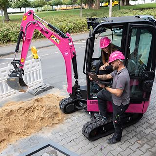 Magenta digger excavating a narrow trench next to a road to lay fiber-optic cable.